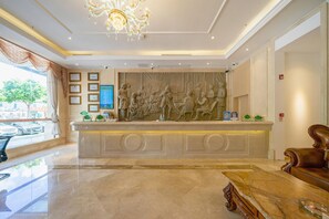 A hotel lobby with a marble reception desk, a chandelier, and a large wall mural. - Vienna Hotel (Shenzhen)