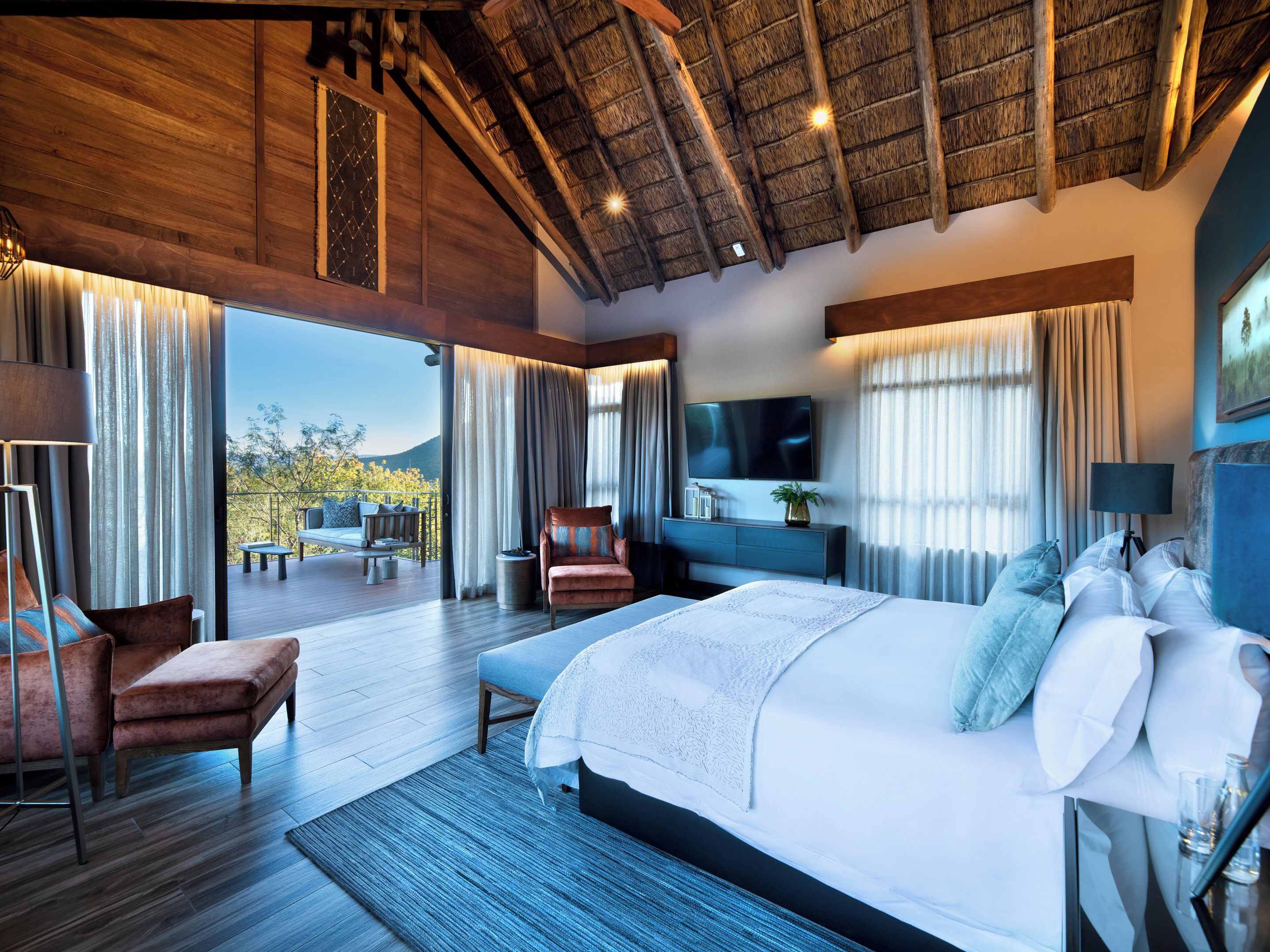 A spacious bedroom with a large bed, a television, and a balcony with outdoor seating.