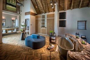 A spacious room with a herringbone wood floor, a large round seating area, a built-in wooden wardrobe, and a stone accent wall. - Babohi at Qwabi Private Game Reserve (Thabazimbi)