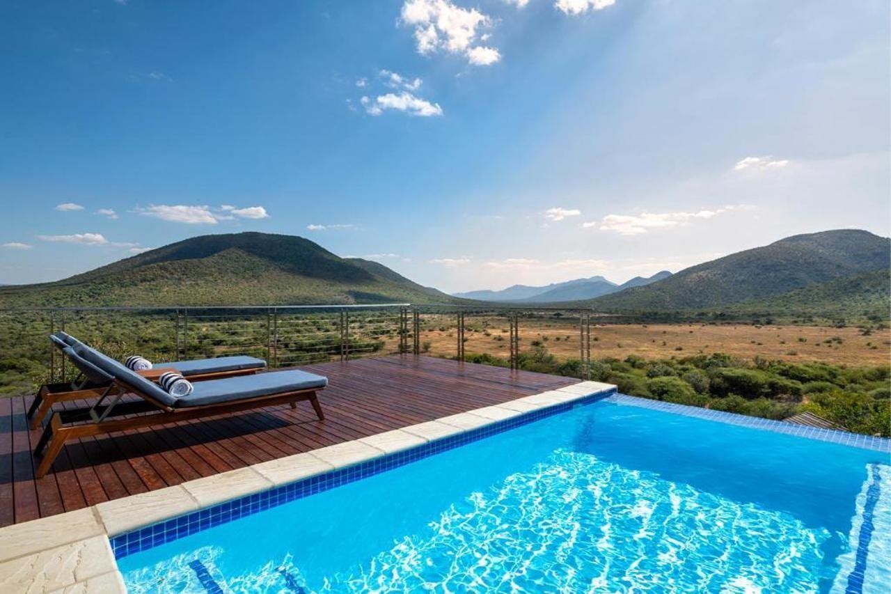 A swimming pool with lounge chairs, surrounded by a wooden deck, with a view of distant mountains.