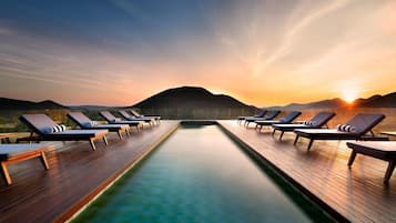 A poolside area with lounge chairs and a view of a mountain at sunset.