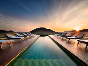 A poolside area with lounge chairs and a view of a mountain at sunset. - Babohi at Qwabi Private Game Reserve (Thabazimbi)
