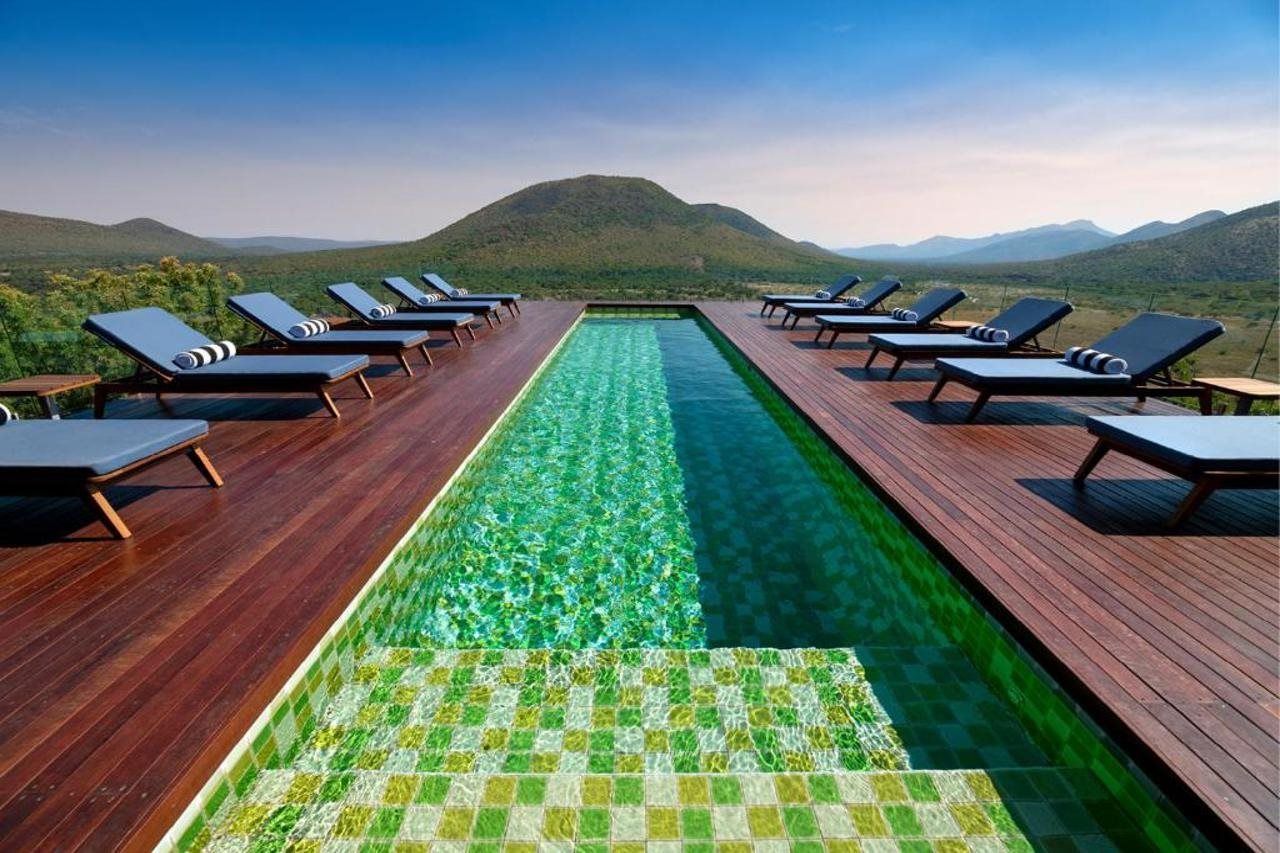 A pool with a clear view of the mountains, surrounded by lounge chairs.
