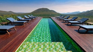 A pool with a clear view of the mountains, surrounded by lounge chairs.