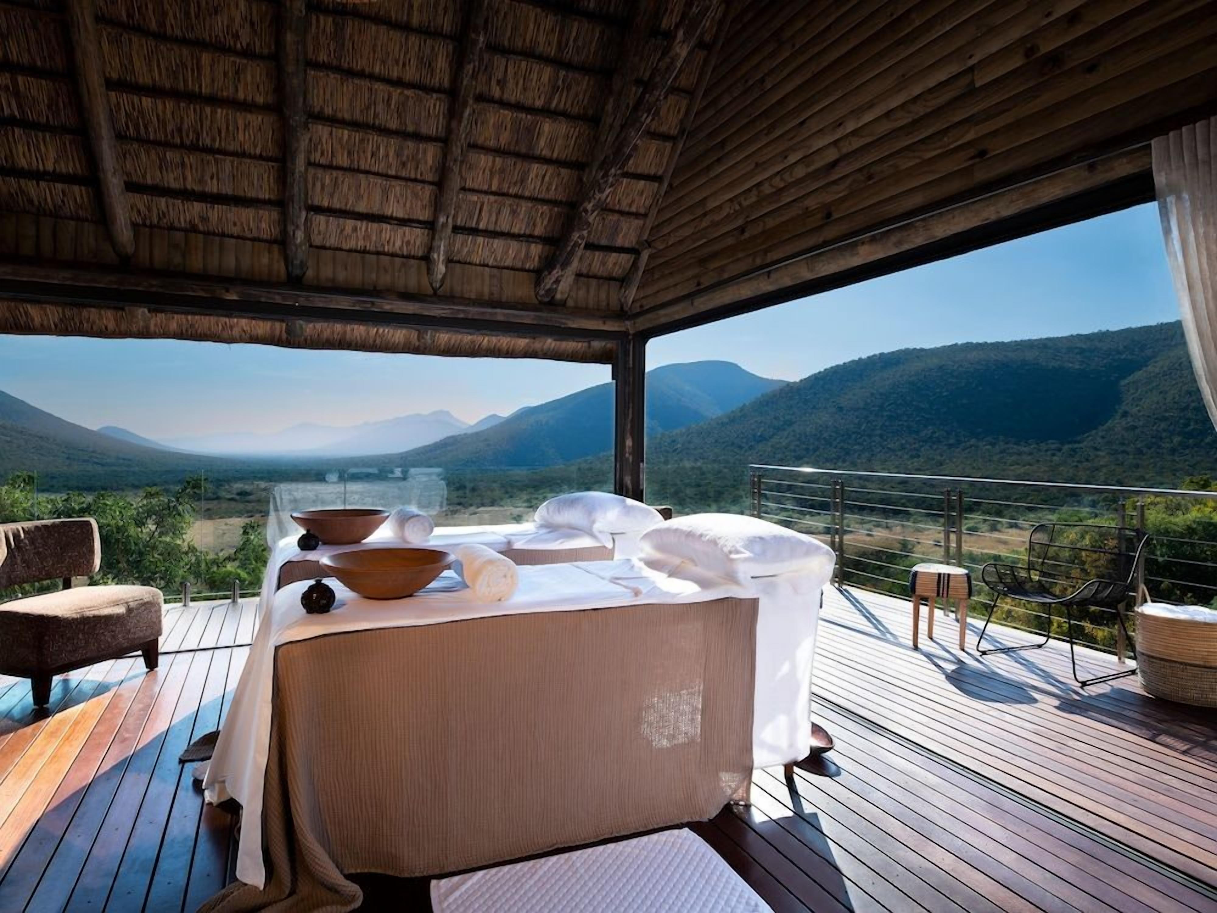 A wooden deck with a thatched roof, a massage table, and a view of a mountainous landscape.