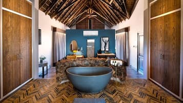 A spacious bathroom with a large bathtub, wooden flooring, and a high ceiling with exposed beams.