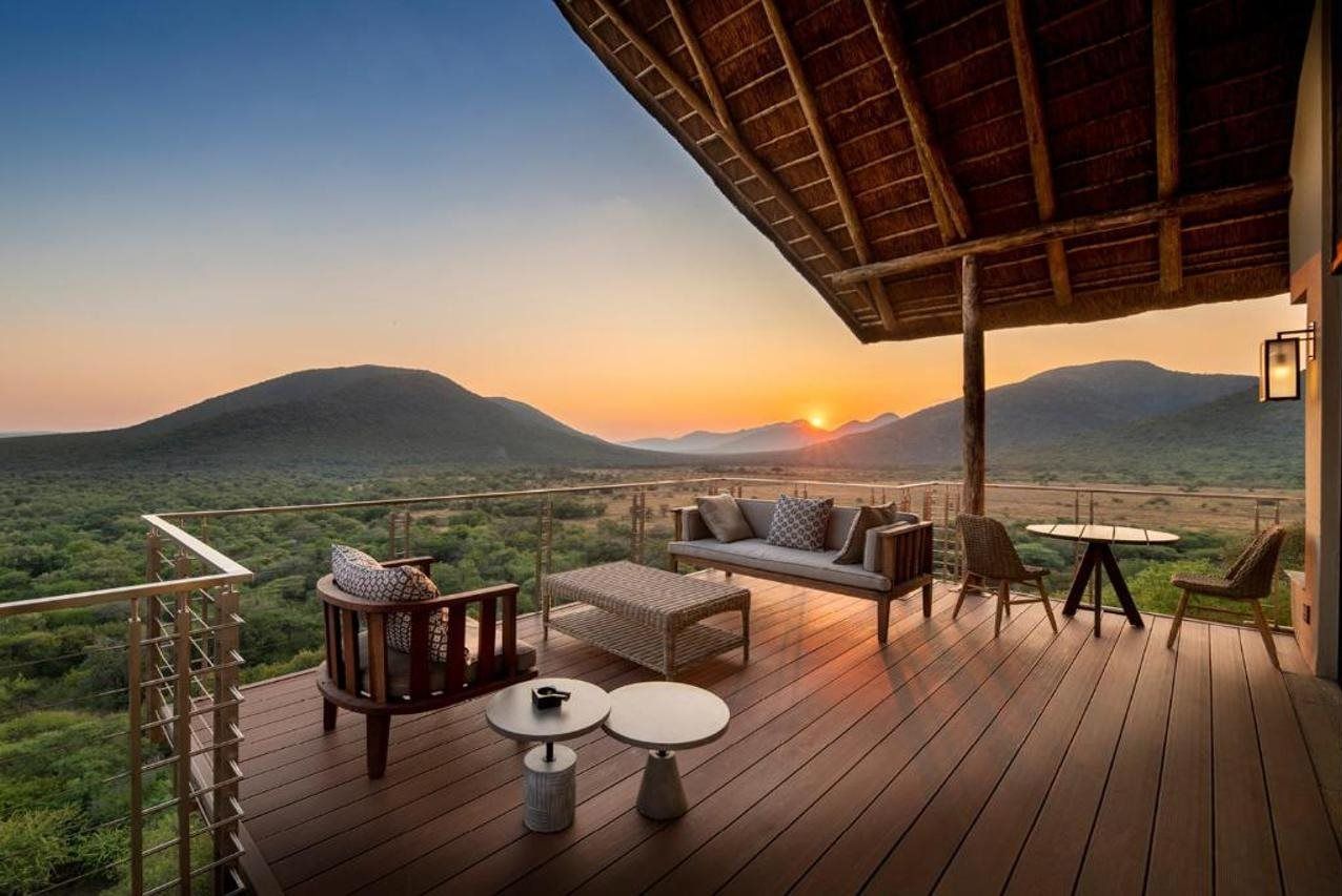 A wooden deck with outdoor furniture, including a sofa, chairs, and tables, overlooking a mountainous landscape.