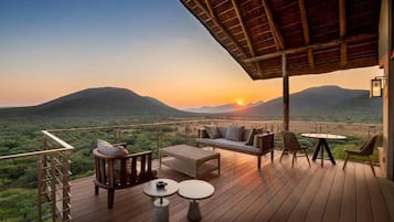 A wooden deck with outdoor furniture, including a sofa, chairs, and tables, overlooking a mountainous landscape.