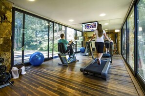 Ett gym med träningsutrustning, stora fönster och en tv.