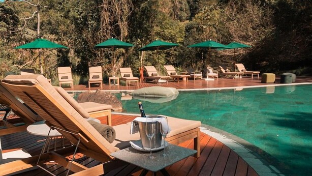Área de piscina com espreguiçadeiras, guarda-sóis e balde de champanhe.