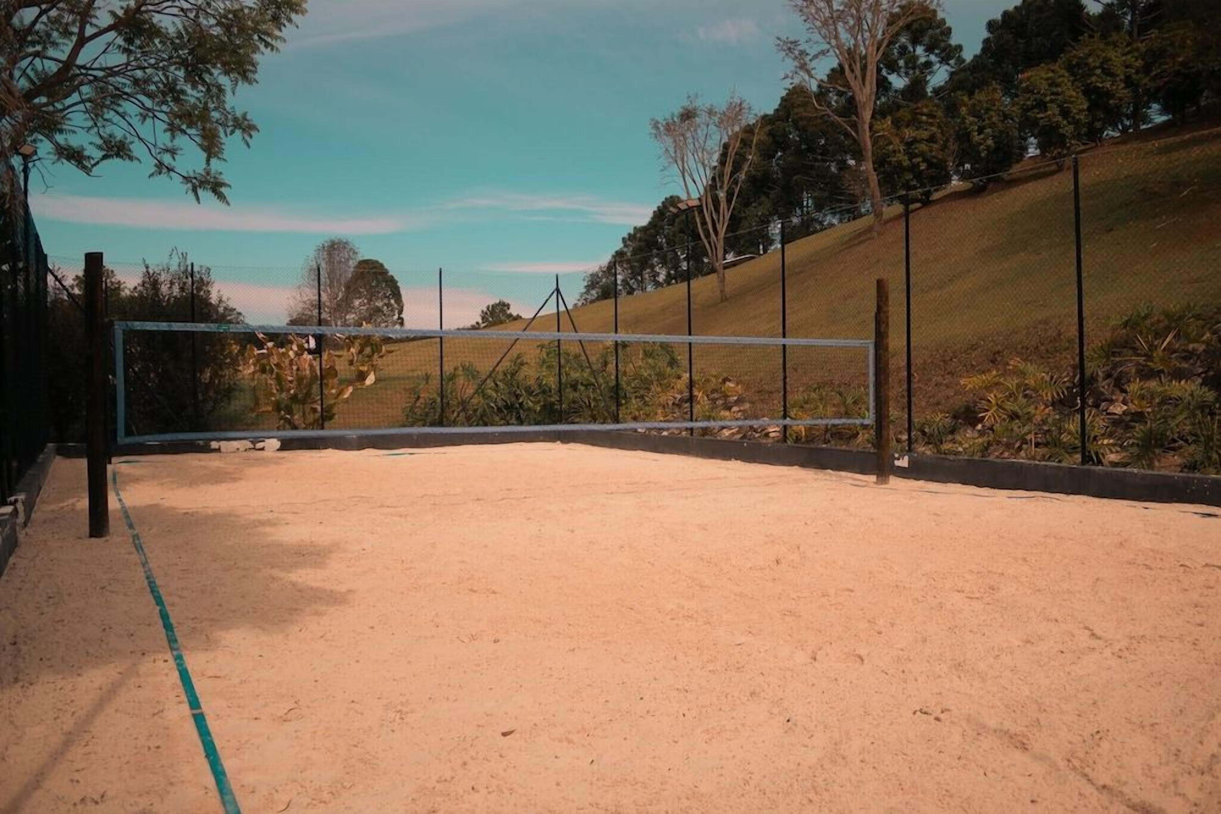Una cancha de voleibol al aire libre con una red, rodeada por una valla y árboles.