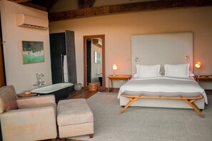 A bedroom with a large bed, a sitting area with chairs, a bathtub, and a mirror.