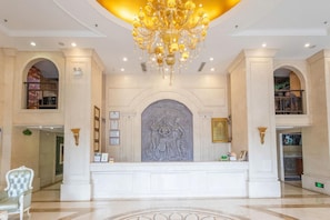 Um hall imponente com um grande lustre, colunas de mármore e uma escultura central.
