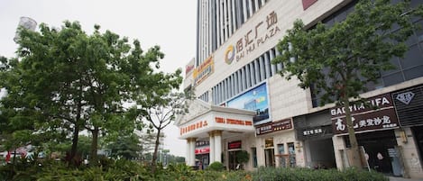 A hotel with a prominent sign, a large tree in front, and several storefronts.