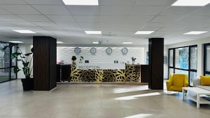 A reception area with a reception desk, clocks, and a large window. - Queen Nelly Park (Kiten)