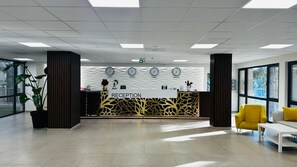 A reception area with a reception desk, clocks, and a large window. - Queen Nelly Park (Kiten)