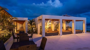 A covered outdoor seating area with tables and chairs, surrounded by plants and a clear sky. - Loisir Terrace and Villas Kouri (Nakijin)