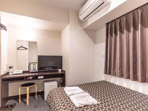 Une chambre d’hôtel équipée d’un lit, d’un bureau avec une télévision, d’un miroir et d’un appareil de climatisation.