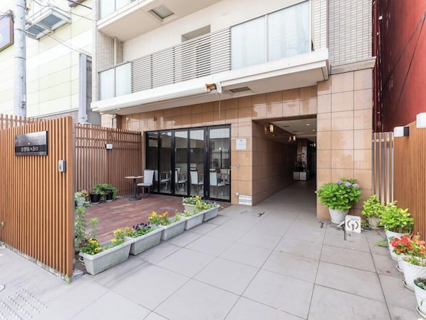 Un bâtiment moderne doté d’une entrée sécurisée par un portail, d’un espace extérieur aménagé avec des sièges et de plantes en pot.