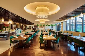 A spacious restaurant with multiple dining tables and chairs, a central chandelier, and large windows providing natural light. - Club Med Joyview Beijing Yanqing (Beijing)