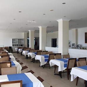 Un grand espace dédié à la salle à manger, avec des tables dressées pour le service, un comptoir avec un présentoir et une vue sur l’extérieur.