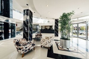 Un hall d’entrée moderne avec des colonnes en marbre, un comptoir d’accueil et des espaces aménagés pour s’asseoir.