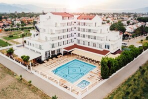 Un hôtel à plusieurs étages doté d’une piscine centrale dans une cour intérieure, entourée de balcons et d’espaces de détente en plein air.