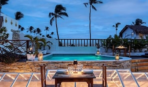 A poolside dining area with a table set for two, surrounded by palm trees and a stone wall. - Mona Lisa Pousada (Jijoca de Jericoacoara)
