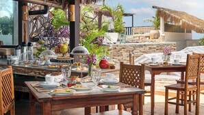 An outdoor dining area with a stone wall backdrop, wooden tables, and chairs. - Mona Lisa Pousada (Jijoca de Jericoacoara)