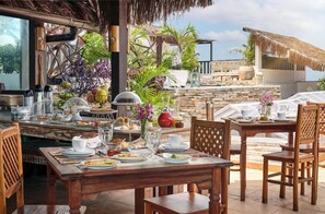 An outdoor dining area with a stone wall backdrop, wooden tables, and chairs. - Mona Lisa Pousada (Jijoca de Jericoacoara)