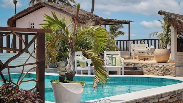 A pool area with lounge chairs, a thatched-roof building, and tropical plants. - Mona Lisa Pousada (Jijoca de Jericoacoara)