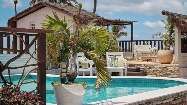 A pool area with lounge chairs, a thatched-roof building, and tropical plants. - Mona Lisa Pousada (Jijoca de Jericoacoara)