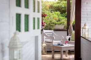 A white interior with a view of a garden. There is a white chair, a table, and a lantern. - Mona Lisa Pousada (Jijoca de Jericoacoara)