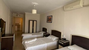 A hotel room with three beds, a desk, a chair, a wardrobe, and a bathroom visible through an open door. - Altinkum Tatil Konaklari (Marmara)