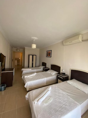 Une chambre d’hôtel avec trois lits, un bureau, une chaise, une armoire et une salle de bain visible à travers une porte ouverte.