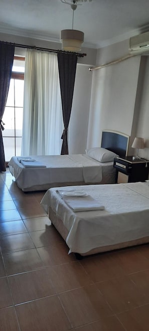 Une chambre d’hôtel avec deux lits, une table de chevet, une lampe et une fenêtre avec des rideaux.