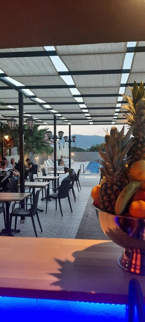 Un espace extérieur aménagé avec des tables et des chaises, une piscine et un panier de fruits posé sur une table.