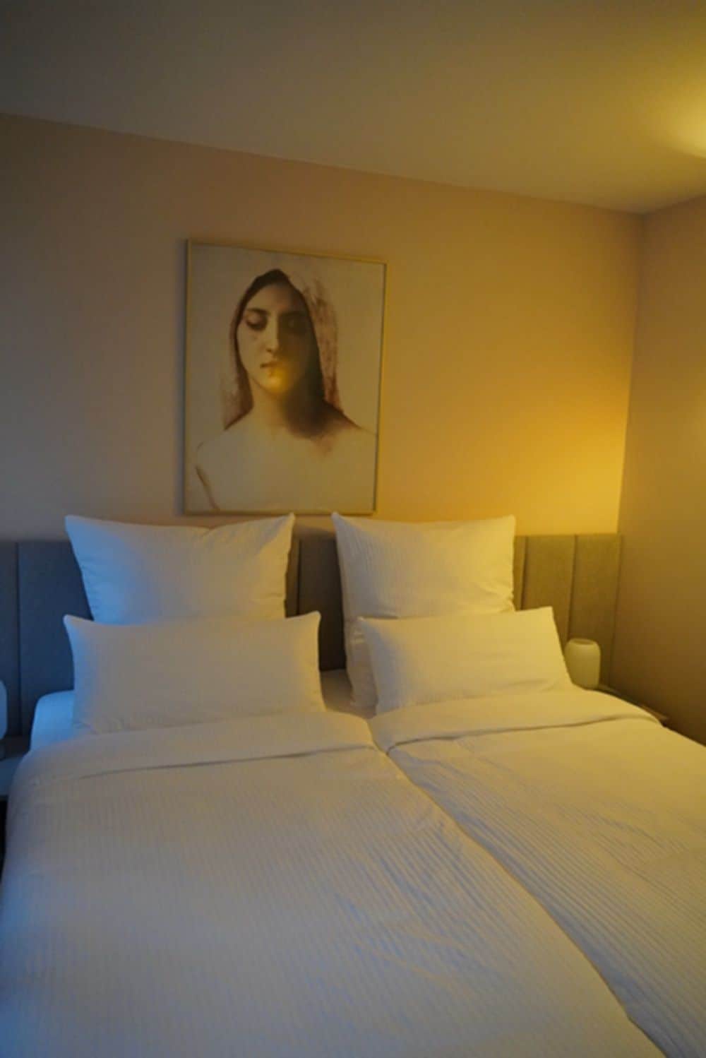 A hotel room with a bed, pillows, a nightstand, and a wall-mounted picture.