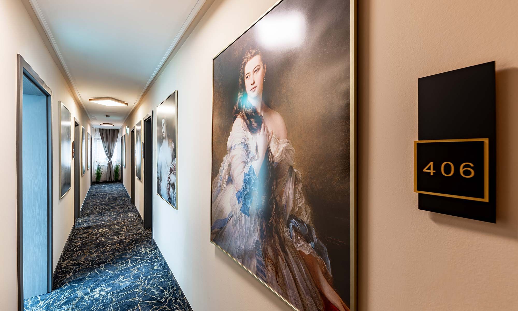 Ein Hotelgang mit Marmorboden, gerahmten Kunstwerken an den Wänden und einem Raumschild.