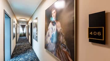 A hotel hallway with a marble floor, framed artwork on the walls, and a room number sign.