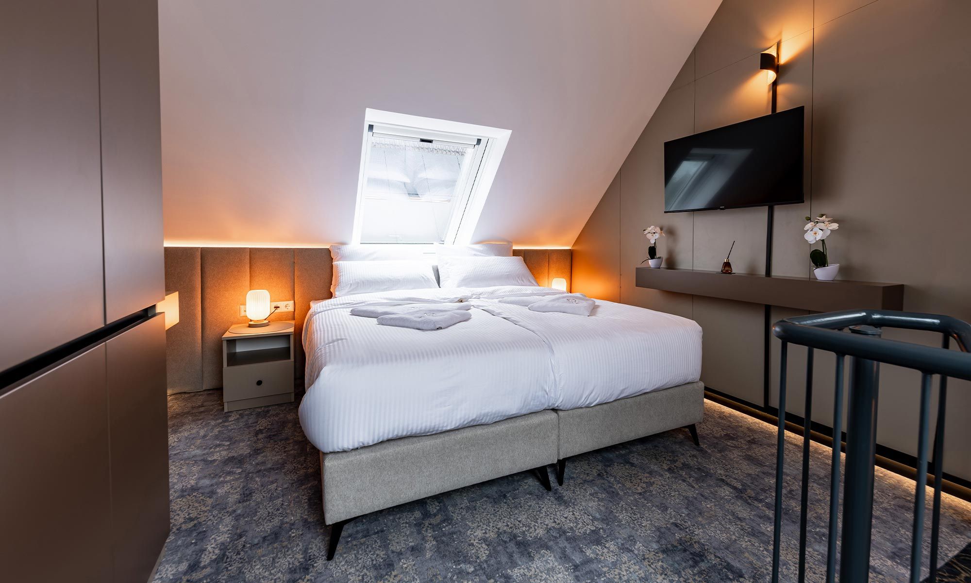 Un dormitorio moderno con cama, lámparas de noche, televisor y ventana.