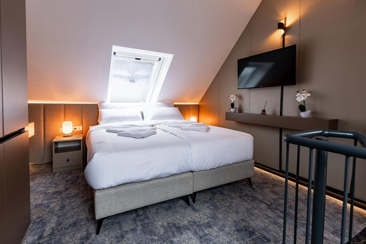 Ein modernes Schlafzimmer mit Bett, Nachttischlampen, Fernseher und Fenster.