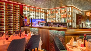 Zona de bar con estantes de botellas y vasos, un reloj y mesas dispuestas para comer.