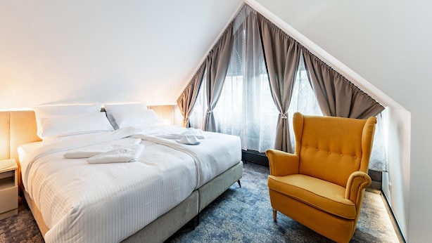 Una habitación de hotel con cama, una silla y una ventana con cortinas.