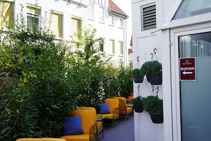 A reception area with a sign indicating the direction to the reception, a row of yellow chairs, and potted plants.