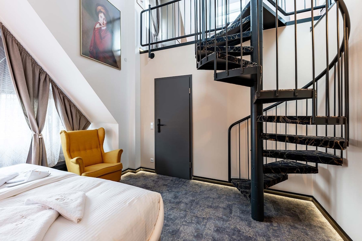Ein Schlafzimmer mit einem Bett, einem Sessel, einer Tür und einer Wendeltreppe.