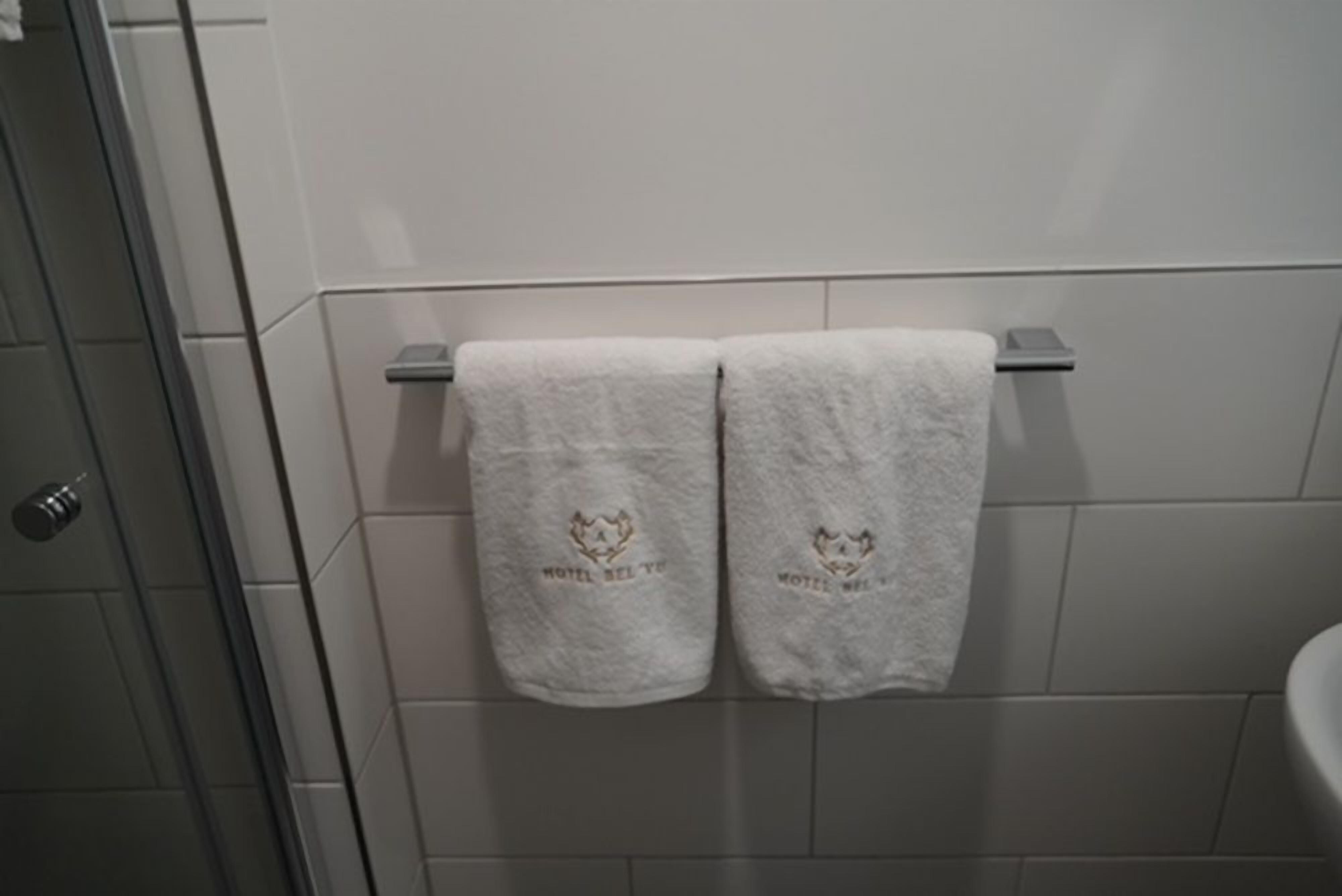 A bathroom with white tiled walls, a towel rack with two towels, and a shower area.