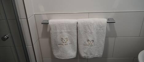 A bathroom with white tiled walls, a towel rack with two towels, and a shower area.