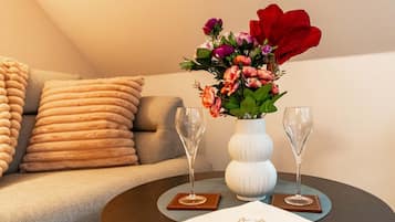 Una habitación con un sofá, un jarrón blanco con flores y dos vasos sobre una mesa redonda.