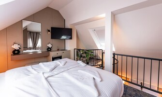 Una habitación de hotel moderna con una cama grande, un televisor de pantalla plana, una kitchenette pequeña y un balcón con plantas.